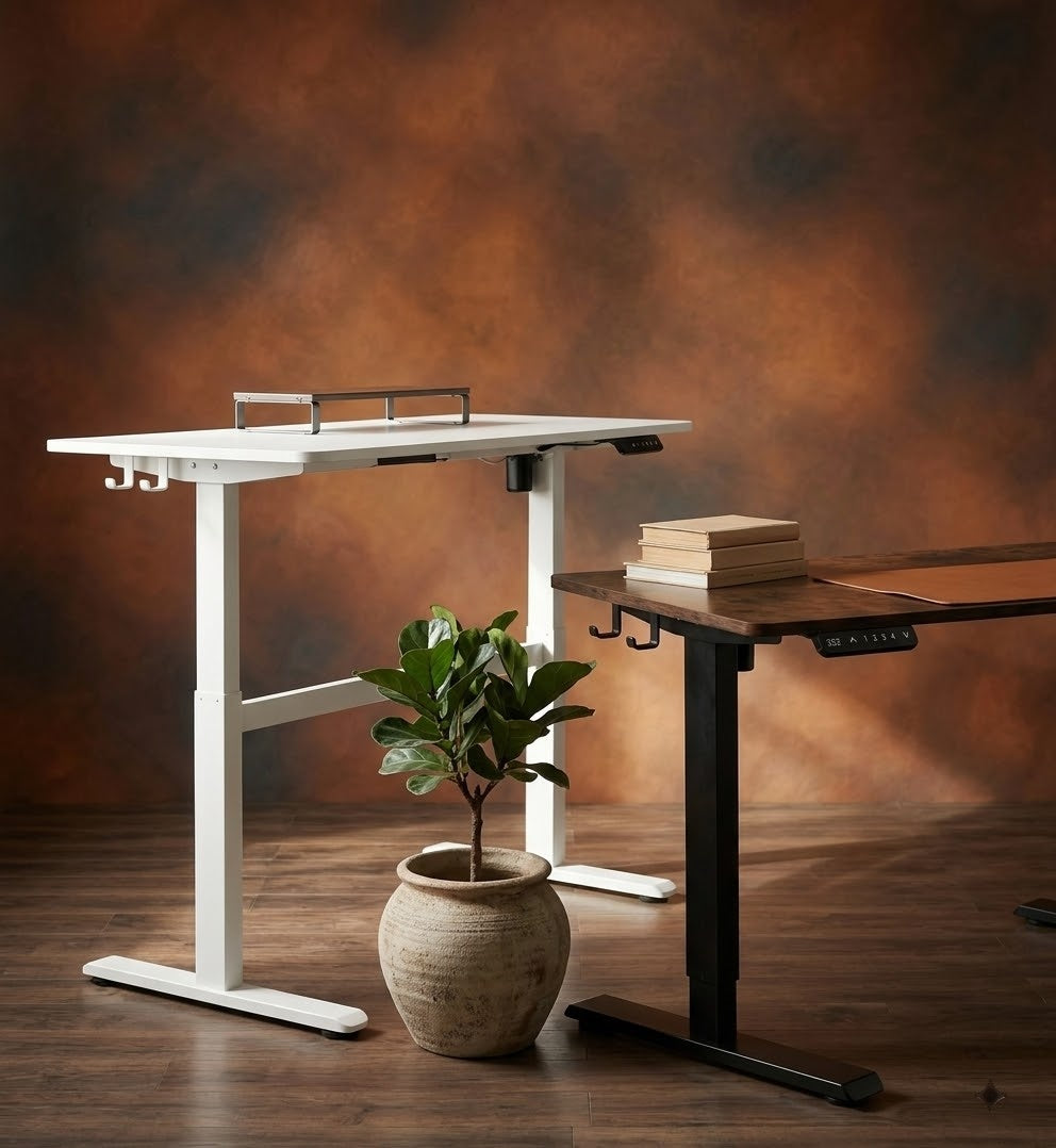 Two Kinetic height-adjustable desks at standing height: a white one in front and a black one behind, against a warm backdrop.